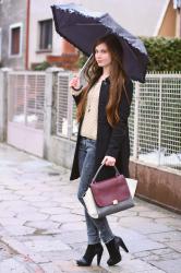 Szare rurki, beżowy sweter, czarny płaszcz i parasol
