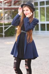 Granatowy płaszcz, czarna sukienka, kapelusz i dziurawe rajstopy