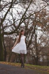 Biała koronkowa sukienka, czarne rajstopy i lakierowane szpilki