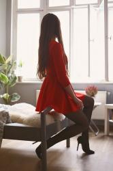 Czerwona sukienka, czarne rajstopy ze szwem i lakierowane szpilki