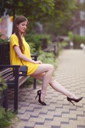 Żółta trapezowa sukienka, czarne szpilki i pikowana torebka