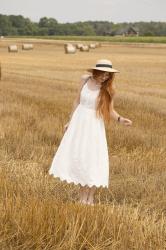 Biała sukienka midi i słomkowy kapelusz w letniej scenerii.