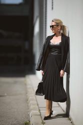 Plisseerock Styling: All Black Outfit mit Midirock, Blazer & Mules.
